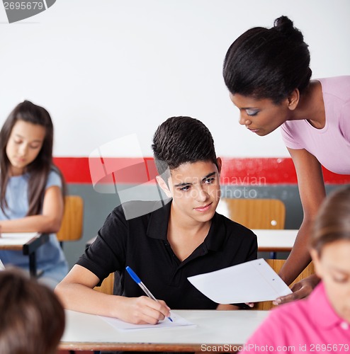 Image of Teacher Showing Paper To Male Student At Desk