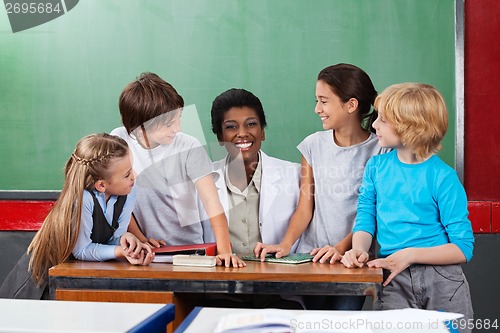 Image of Teacher Sitting At Desk With Students At Desk