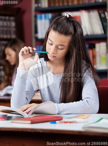 Image of Schoolgirl Holding Pen While Reading Book In Library