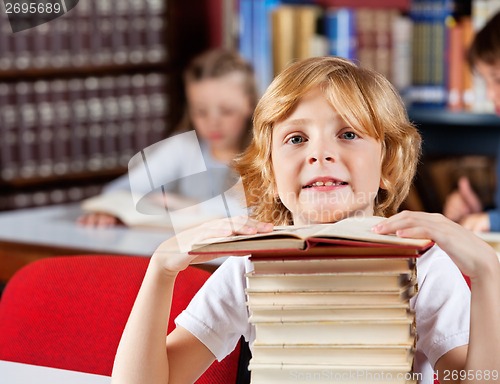 Image of Schoolboy With Stack Of Books Sitting In Library