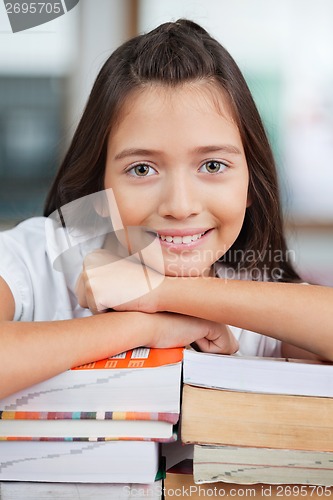 Image of Schoolgirl Leaning On Stack Of Books In Classroom