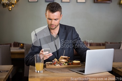 Image of Businessman Messaging On Cellphone While Having Sandwich