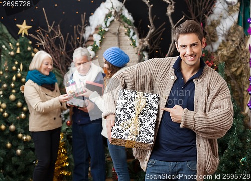 Image of Man Pointing At Christmas Present With Family In Background