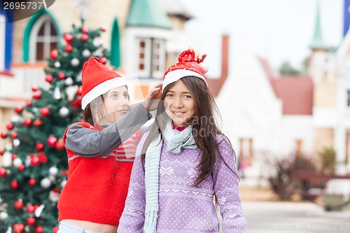 Image of Girl Smiling While Friend Putting Santa Hat On Her Head