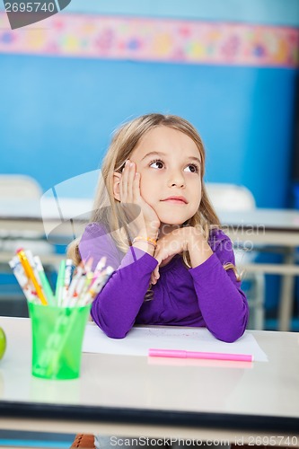 Image of Girl With Hand On Chin Sitting At Desk In Kindergarten