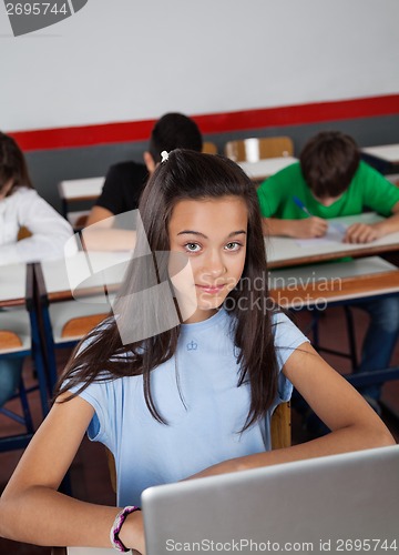 Image of Pretty Teenage Schoolgirl Sitting With Laptop In Classroom