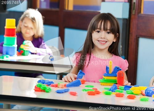Image of Girl With Construction Block While Friend Playing In Background
