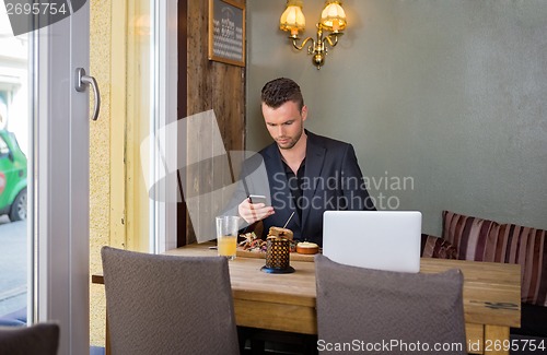 Image of Business man Messaging On Cellphone While Having Food