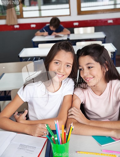 Image of Schoolgirl Sitting With Classmate At Desk In Classroom