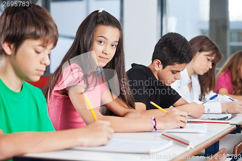 Image of Teenage Girl Sitting With Classmates Writing At Desk