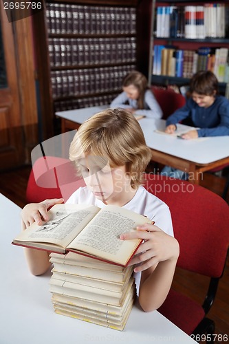 Image of Schoolboy With Stacked Books Reading In Library