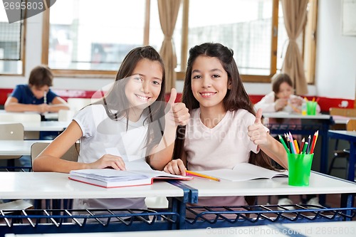 Image of Happy Schoolgirls Gesturing Thumbs Up At Desk