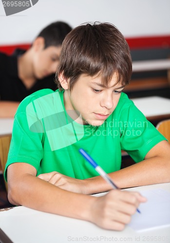 Image of Teenage Schoolboy Writing At Desk During Examination