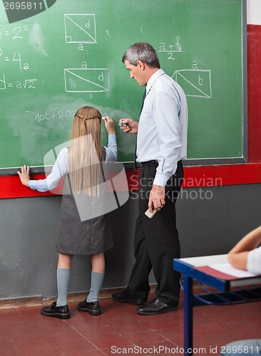 Image of Little Girl Writing On Board With Teacher Assisting Her