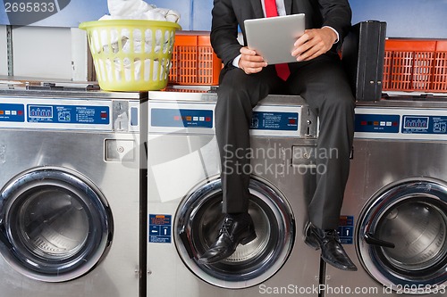 Image of Businessman Using Digital Tablet While Sitting On Washing Machin