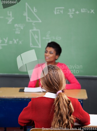 Image of Schoolgirl Sitting At Desk With Teacher In Background