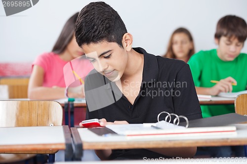 Image of Teenage Schoolboy Text Messaging At Desk