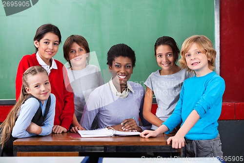 Image of Teacher And Schoolchildren Smiling Together At Desk In Classroom