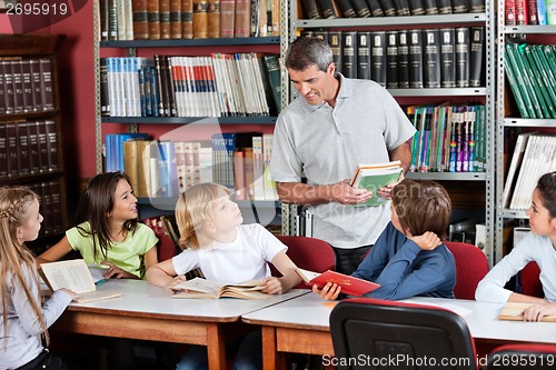 Image of Teacher Communicating With Students Sitting At Table In Library