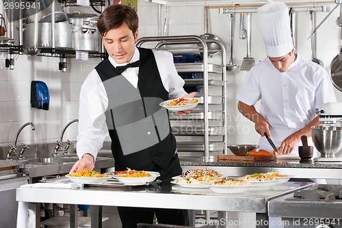 Image of Waiter And Chef Working In Commercial Kitchen