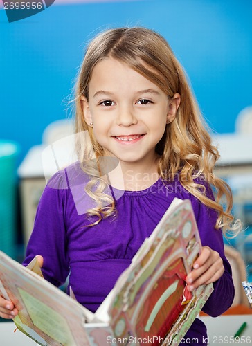 Image of Girl Smiling While Holding Book In Kindergarten