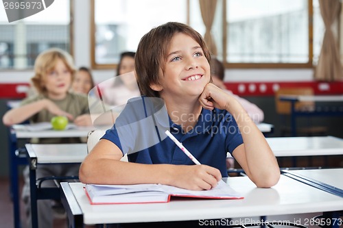 Image of Schoolboy Looking Up While Studying At Desk