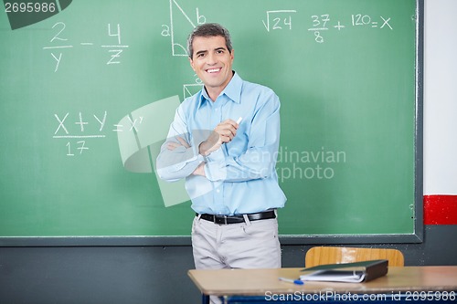 Image of Male Teacher Standing Arms Crossed Against Board