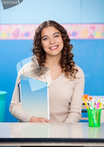 Image of Teacher Holding Book While Sitting At Desk