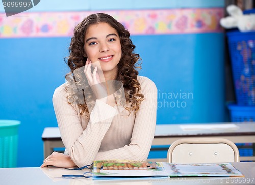 Image of Teacher With Hand On Chin Sitting At Desk