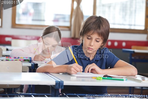 Image of Little Boy Writing Notes With Classmate In Background