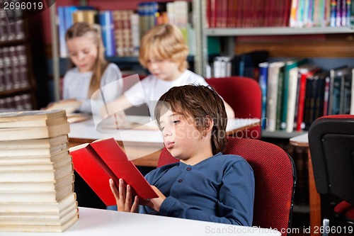 Image of Relaxed Schoolboy Reading Book In Library