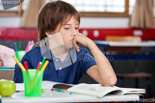 Image of Schoolboy Looking At Book In Classroom