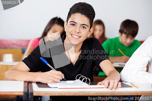 Image of Teenage Schoolboy Writing In Binder At Desk