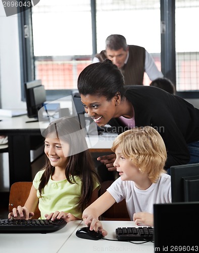 Image of Teacher Assisting Schoolchildren In Using Desktop Pc