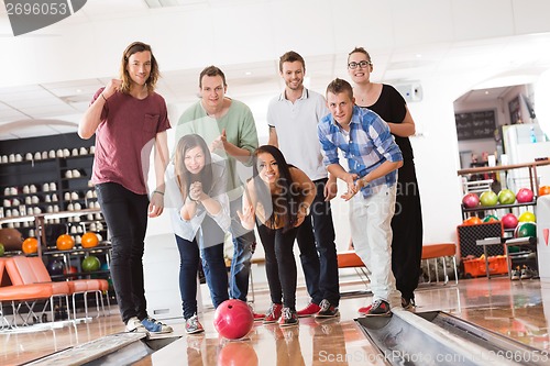 Image of Woman Bowling While Friends Cheering in Club