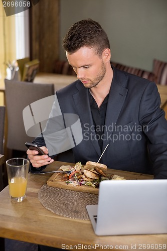 Image of Businessman Using Mobilephone While Having Food