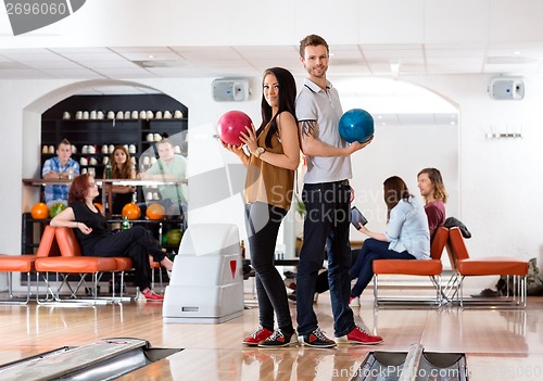 Image of Young Man And Woman Holding Bowling Balls in Club