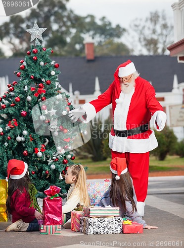 Image of Santa Claus Gesturing At Children By Christmas Tree