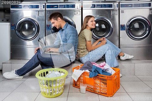 Image of Couple Using Laptop And Earphones At Laundry