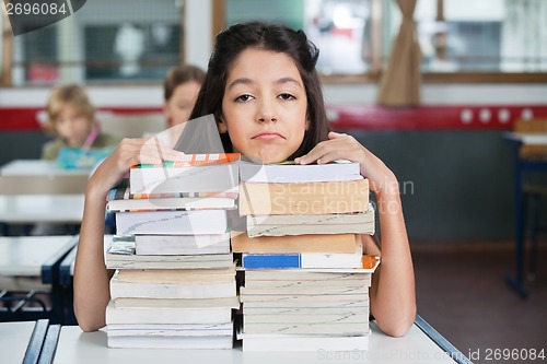 Image of Sad Schoolgirl Resting Chin On Stacked Books At Desk