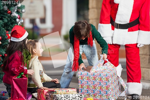 Image of Boy Opening Christmas Present In Courtyard