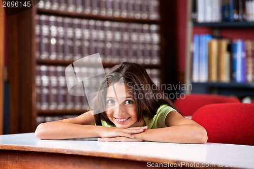 Image of Happy Schoolgirl Resting Chin On Hands At Table In Library