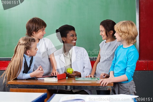 Image of Schoolchildren Looking Teacher Sitting At Desk