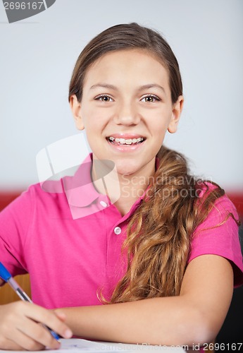 Image of Happy Teenage Schoolgirl Writing At Desk