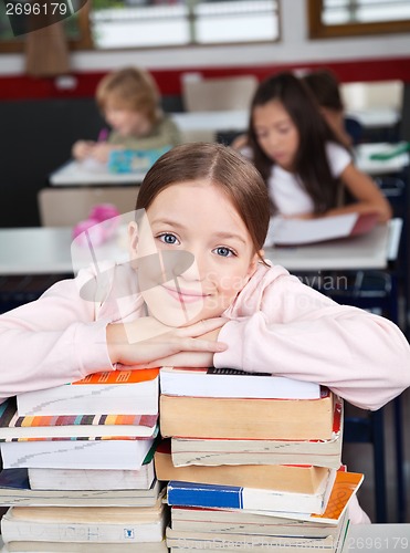 Image of Happy Schoolgirl Leaning On Stacked Books At Desk