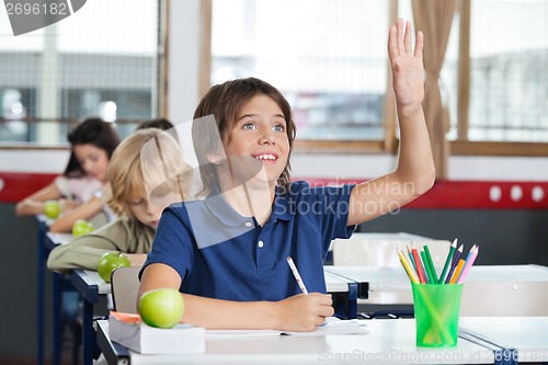 Image of Schoolboy Raising Hand While Sitting At Desk