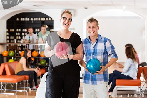 Image of Happy Man And Woman Holding Bowling Balls in Club