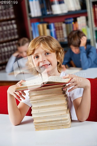 Image of Schoolboy Smiling While Sitting With Stack Of Books In Library