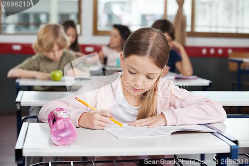 Image of Schoolgirl Drawing In Book At Classroom