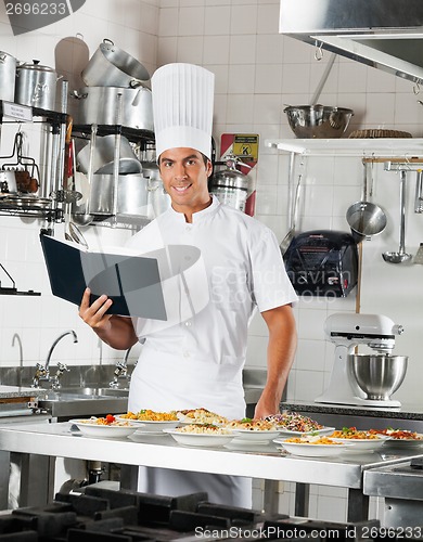 Image of Chef With Book Standing By Kitchen Counter